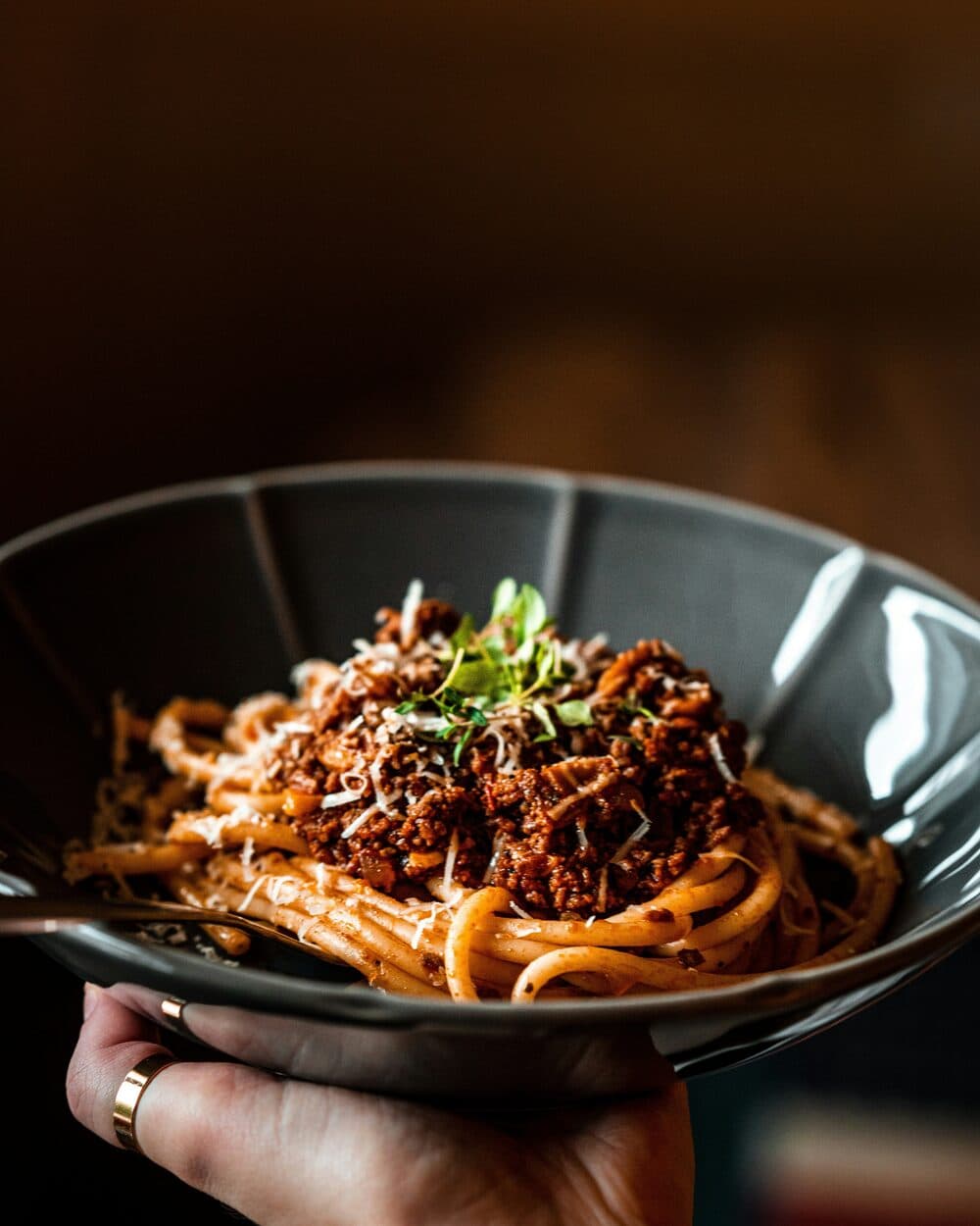 Djup skål med pasta bolognese toppad med riven parmesan och färska örter